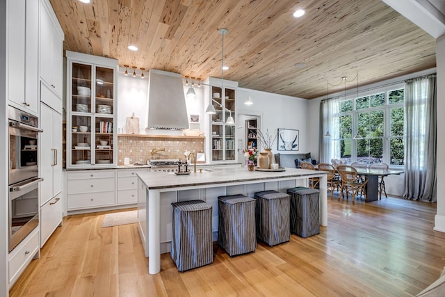 kitchen with decorative light fixtures, wood ceiling, an island with sink, and range hood