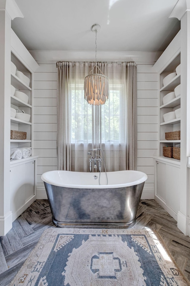 bathroom featuring wood walls, parquet flooring, a tub to relax in, and an inviting chandelier