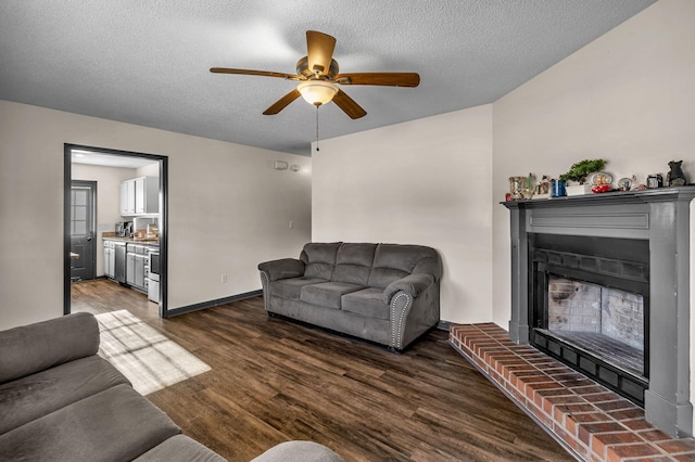 living room with dark hardwood / wood-style flooring, ceiling fan, a fireplace, and a textured ceiling