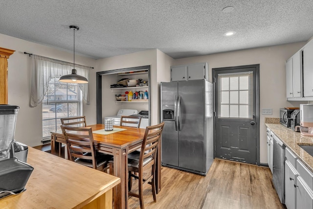 kitchen with stainless steel appliances, independent washer and dryer, light stone counters, decorative light fixtures, and light wood-type flooring