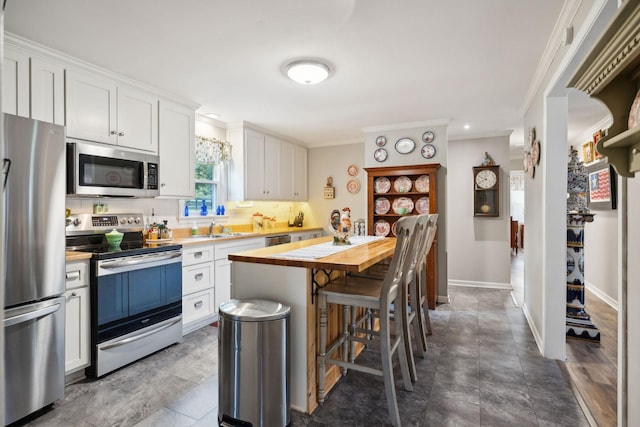 kitchen with white cabinetry, wood counters, crown molding, a kitchen bar, and appliances with stainless steel finishes