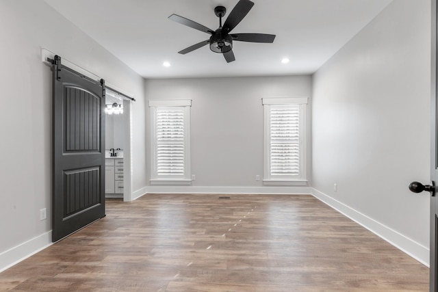 spare room featuring ceiling fan, a barn door, and light wood-type flooring