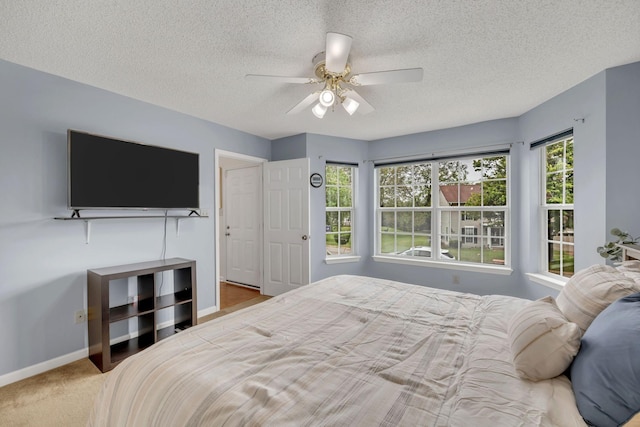 bedroom featuring a textured ceiling, ceiling fan, light carpet, and multiple windows