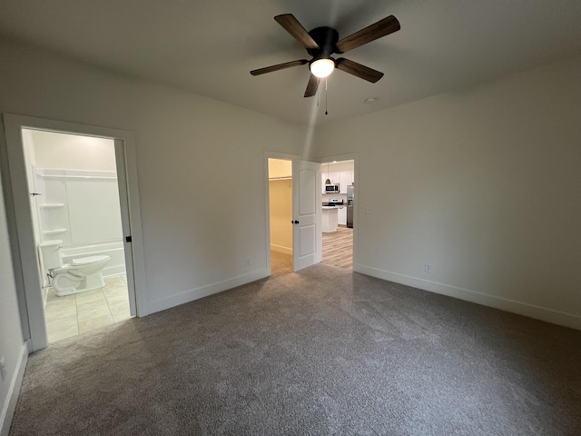 unfurnished bedroom featuring connected bathroom, ceiling fan, a walk in closet, light carpet, and a closet