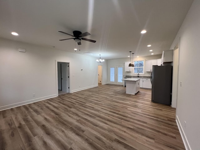 unfurnished living room featuring ceiling fan with notable chandelier, dark wood-type flooring, and sink