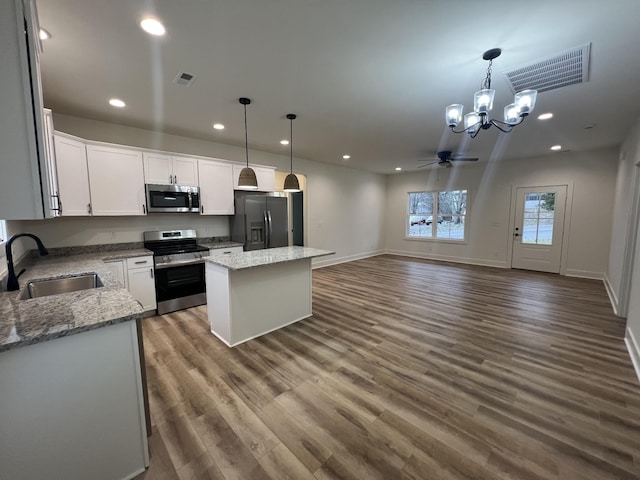 kitchen with sink, stainless steel appliances, a kitchen island, decorative light fixtures, and white cabinets