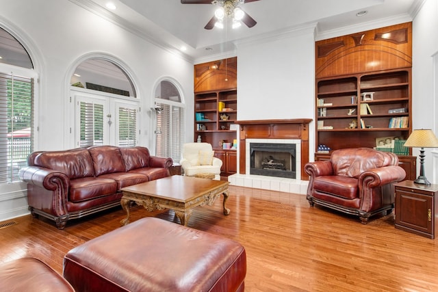 living room featuring built in shelves, ceiling fan, ornamental molding, a fireplace, and light hardwood / wood-style floors