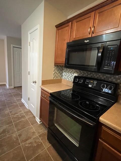 kitchen featuring backsplash, dark tile patterned floors, and black appliances