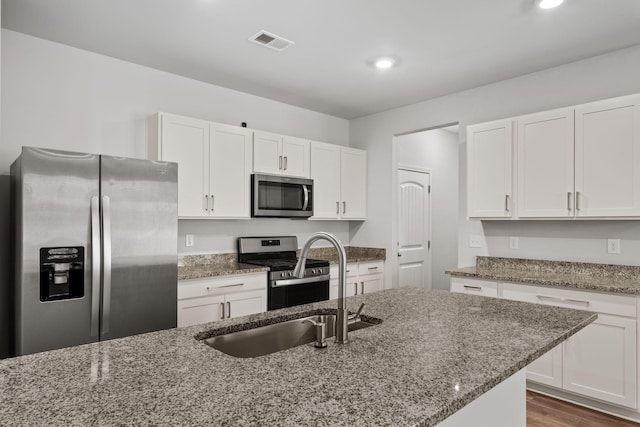 kitchen featuring white cabinets, stone counters, an island with sink, and appliances with stainless steel finishes