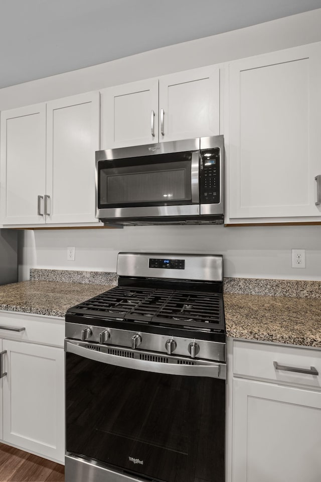 kitchen featuring dark stone countertops, white cabinetry, dark hardwood / wood-style flooring, and appliances with stainless steel finishes