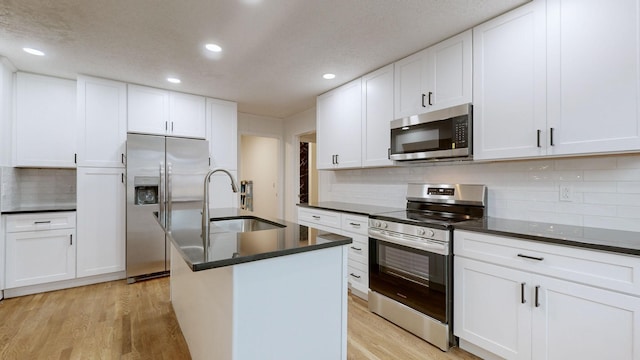 kitchen with white cabinets, stainless steel appliances, a kitchen island with sink, and sink