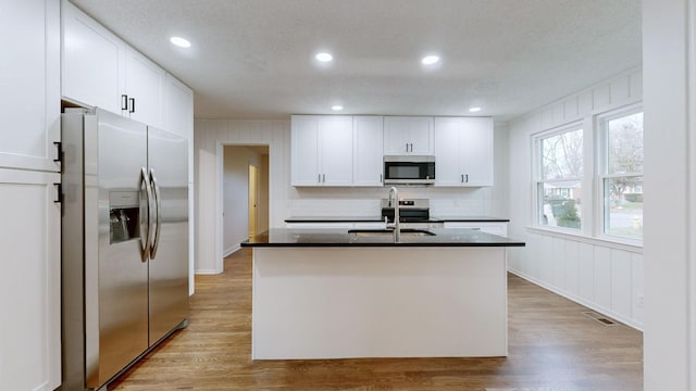 kitchen featuring white cabinetry, sink, stainless steel appliances, light hardwood / wood-style floors, and a center island with sink