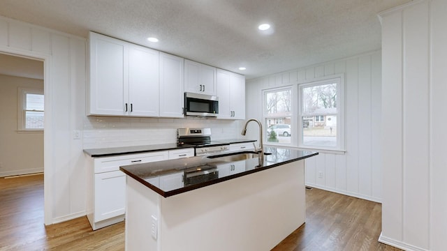 kitchen featuring stainless steel appliances, white cabinetry, a kitchen island with sink, and sink