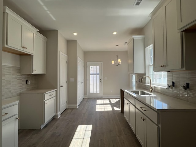 kitchen with a sink, a healthy amount of sunlight, white cabinets, light countertops, and dark wood finished floors