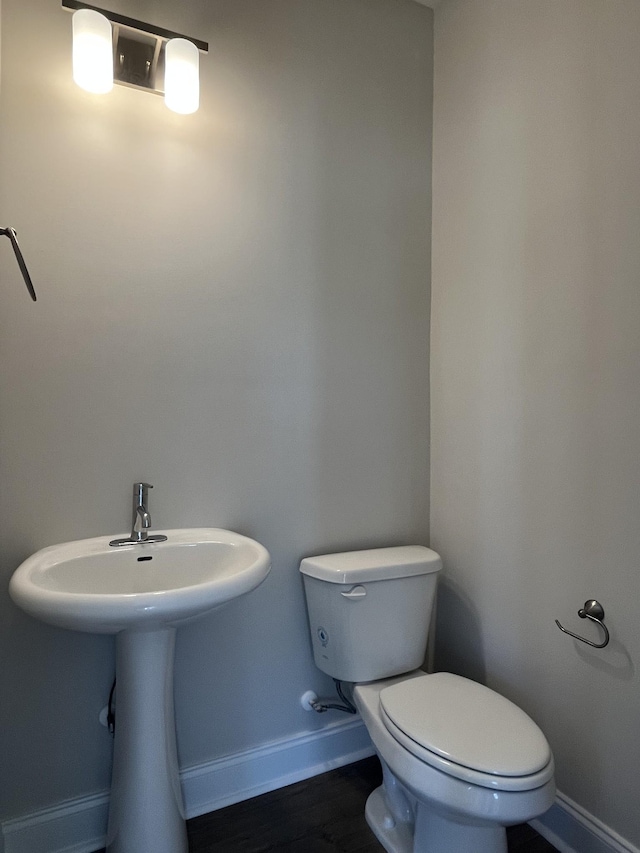 half bathroom featuring baseboards, toilet, and wood finished floors