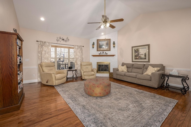 living room with a brick fireplace, dark hardwood / wood-style flooring, vaulted ceiling, and ceiling fan