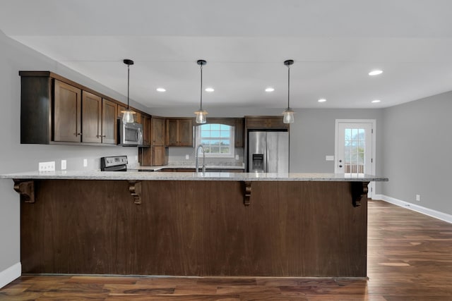 kitchen with light stone countertops, dark wood-type flooring, pendant lighting, and appliances with stainless steel finishes