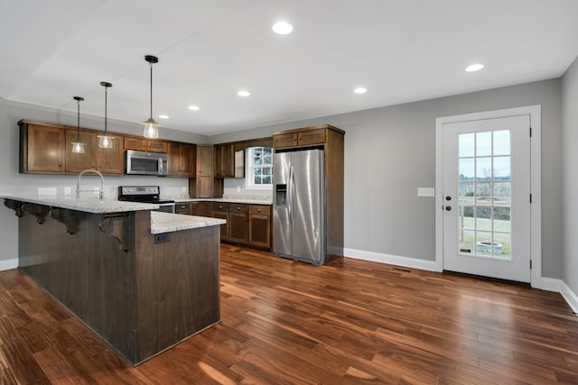 kitchen featuring kitchen peninsula, a kitchen bar, dark hardwood / wood-style flooring, stainless steel appliances, and pendant lighting