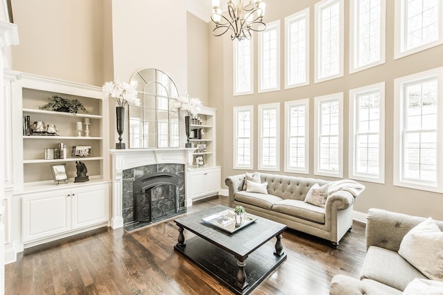 living room featuring a high end fireplace, built in shelves, a notable chandelier, a high ceiling, and dark hardwood / wood-style floors