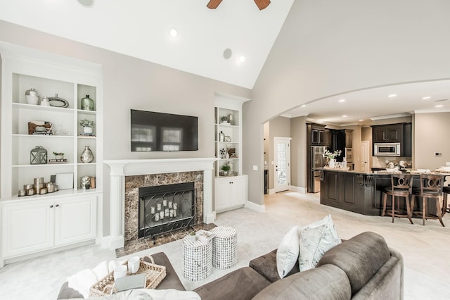 living room featuring built in shelves, ceiling fan, a fireplace, and high vaulted ceiling