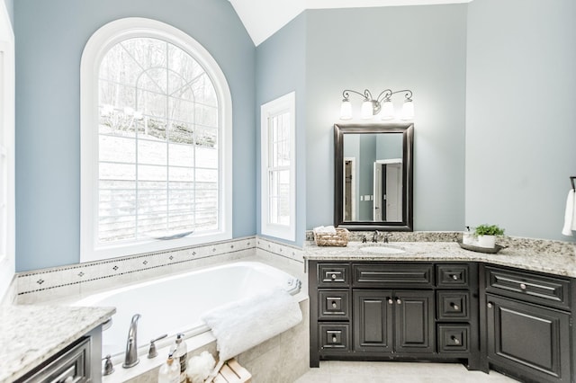 bathroom featuring vanity, a relaxing tiled tub, and vaulted ceiling