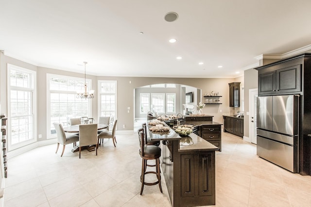 kitchen with ornamental molding, decorative light fixtures, a center island with sink, a notable chandelier, and stainless steel refrigerator