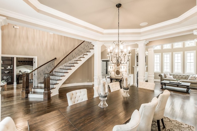 dining space featuring a raised ceiling, ornate columns, a chandelier, and ornamental molding