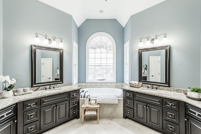 bathroom featuring vanity, a relaxing tiled tub, and vaulted ceiling