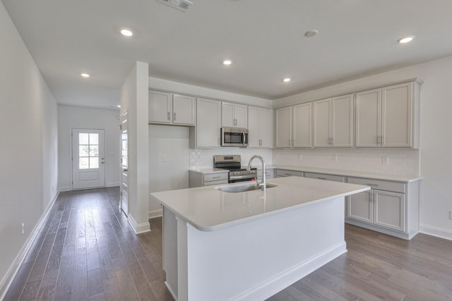 kitchen with appliances with stainless steel finishes, light wood-type flooring, backsplash, a kitchen island with sink, and sink