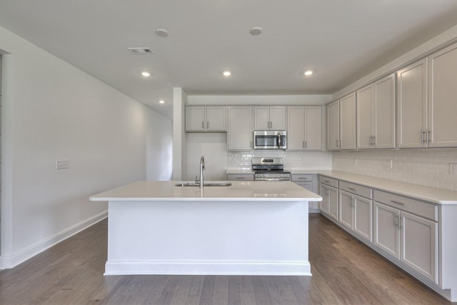 kitchen with sink, gray cabinets, an island with sink, tasteful backsplash, and stainless steel appliances