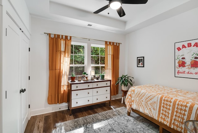 bedroom featuring a raised ceiling, ceiling fan, a closet, and dark wood-type flooring