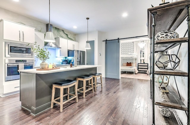 kitchen featuring a barn door, stainless steel appliances, dark hardwood / wood-style flooring, pendant lighting, and white cabinets