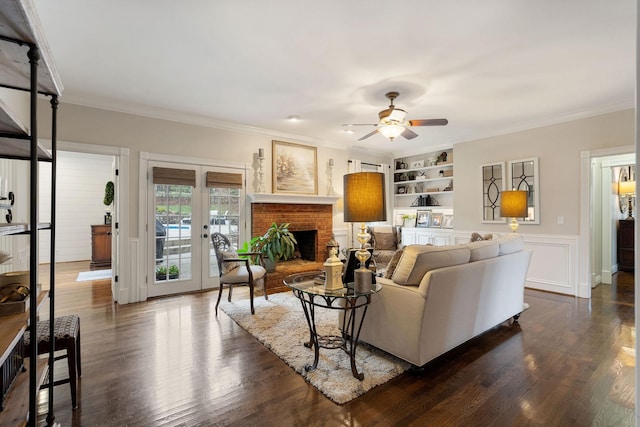 living room featuring built in shelves, ceiling fan, french doors, a brick fireplace, and crown molding