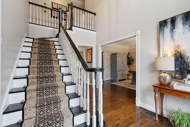 staircase with wood-type flooring, ornamental molding, and a high ceiling