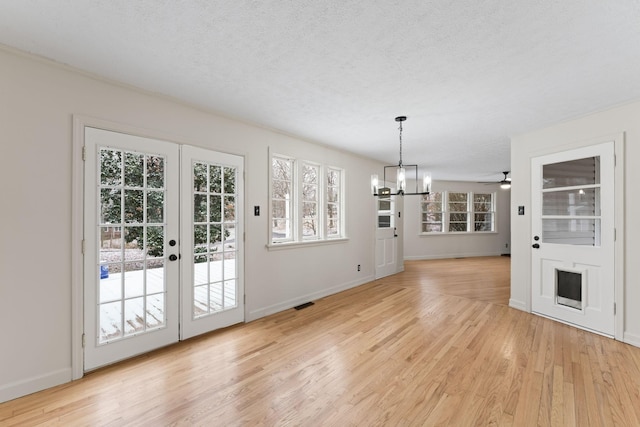 interior space featuring a textured ceiling, ceiling fan with notable chandelier, light hardwood / wood-style floors, and french doors