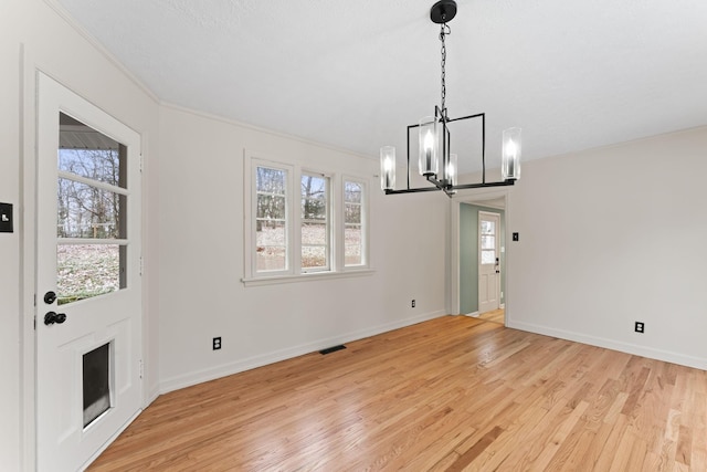 unfurnished dining area featuring light hardwood / wood-style floors, ornamental molding, a wealth of natural light, and an inviting chandelier