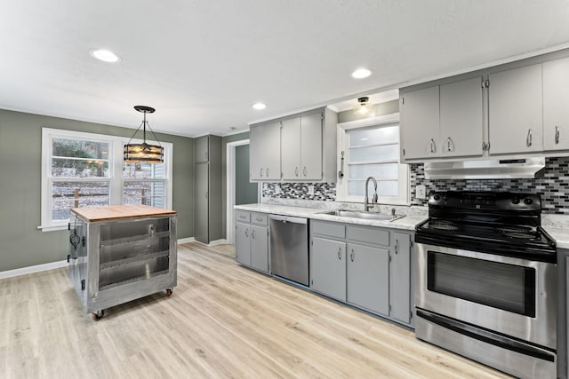 kitchen with sink, hanging light fixtures, gray cabinets, light wood-type flooring, and stainless steel appliances