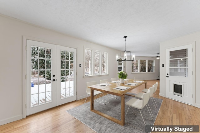 dining area featuring ceiling fan with notable chandelier, light wood-type flooring, a textured ceiling, and french doors