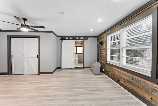 interior space featuring ceiling fan, crown molding, wooden walls, a barn door, and light hardwood / wood-style flooring