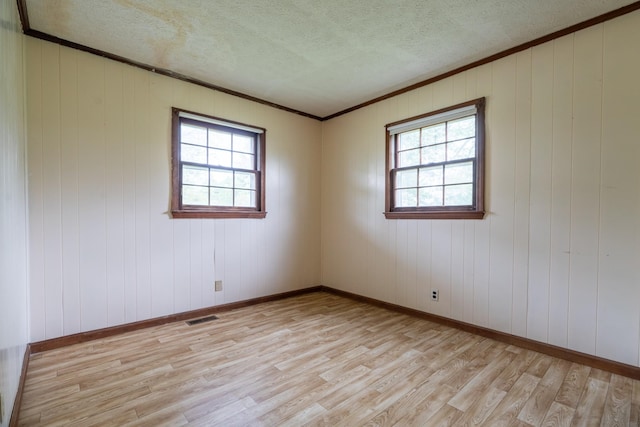 empty room with wood walls, ornamental molding, a textured ceiling, and light wood-type flooring