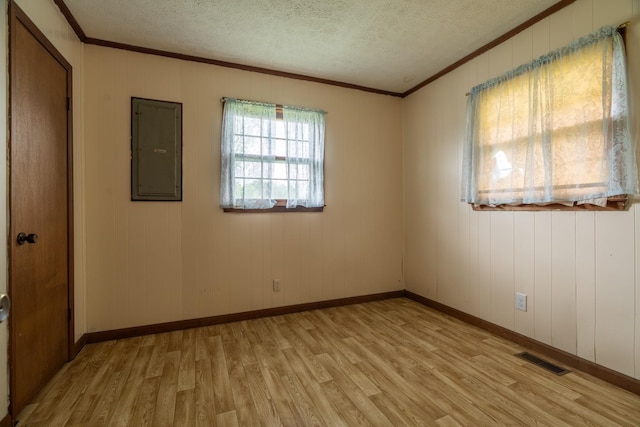 spare room with light hardwood / wood-style floors, ornamental molding, a textured ceiling, and electric panel