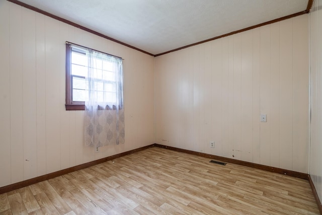 empty room featuring wooden walls, light hardwood / wood-style floors, and crown molding