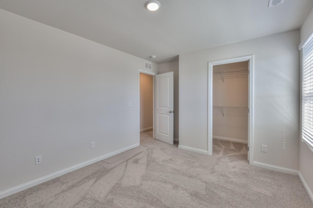 unfurnished bedroom featuring a spacious closet, light carpet, and a closet