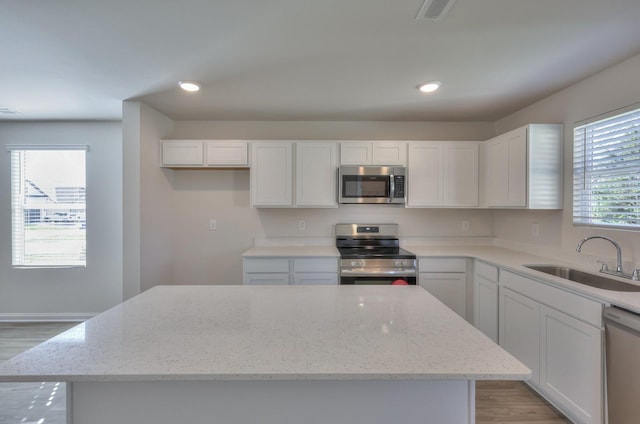 kitchen with a center island, appliances with stainless steel finishes, sink, and light stone counters