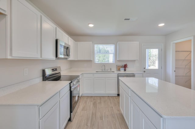 kitchen with stainless steel appliances, sink, white cabinets, and light hardwood / wood-style flooring