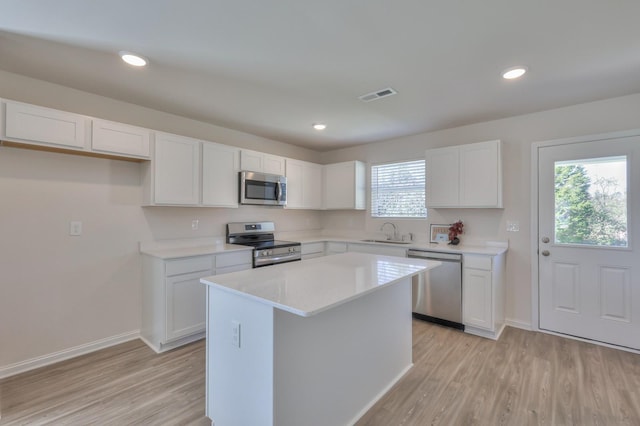 kitchen with light hardwood / wood-style flooring, stainless steel appliances, white cabinets, and a kitchen island