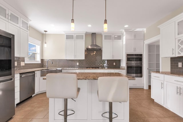 kitchen with a sink, a kitchen island, stainless steel appliances, a breakfast bar area, and wall chimney range hood