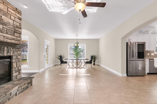 unfurnished dining area with light tile patterned floors, a fireplace, a ceiling fan, and baseboards