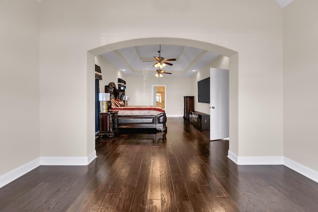 bedroom with arched walkways, baseboards, a tray ceiling, and wood finished floors