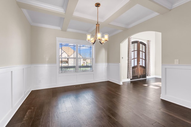 empty room with dark wood finished floors, an inviting chandelier, arched walkways, and beam ceiling